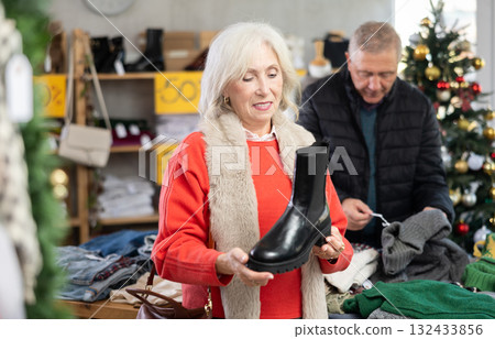 Mature woman standing on the background of a Christmas tree and choosing platform boots Mature woman standing on the background of a Christmas tree and choosing platform boots 132433856