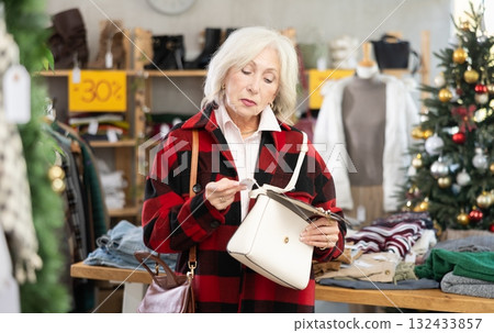 Mature woman standing and choosing handbag on Christmas tree background Mature woman standing and choosing handbag on Christmas tree background 132433857