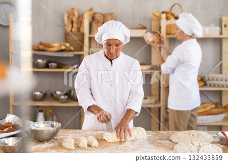 Senior woman baker cutting dough into pieces Senior woman baker cutting dough into pieces 132433859