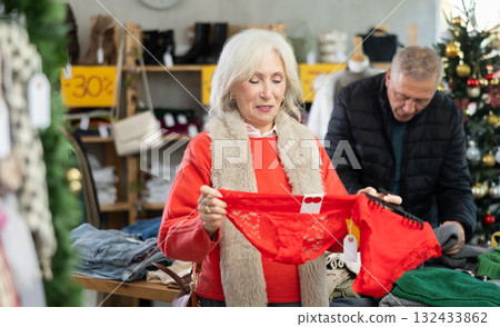 Elderly female shopper selects red panties in fashionable clothing boutique Elderly female shopper selects red panties in fashionable clothing boutique 132433862