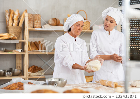 Elderly female baker giving advice to young assistant in kitchen 132433871