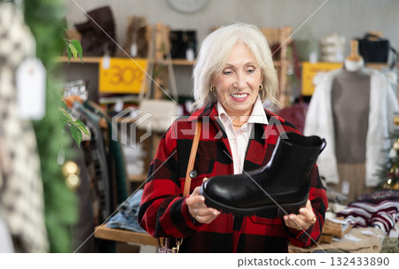 Happy elderly woman chooses fashionable platform boots in shoe store Happy elderly woman chooses fashionable platform boots in shoe store 132433890