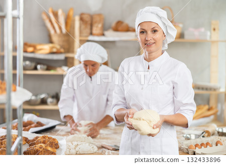 Smiling female baker holding ball of dough in bakery Smiling female baker holding ball of dough in bakery 132433896