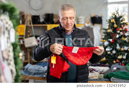 Attentive mature man choosing red panties in clothing store 132433952