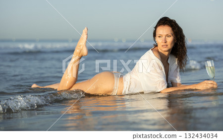 Topless woman in shirt with champagne on coast 132434034