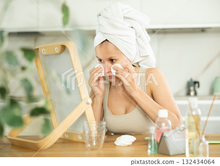 Middle-aged woman cleaning her facial skin with cotton disks sitting in front of the mirror Middle-aged woman cleaning her facial skin with cotton disks sitting in front of the mirror 132434064