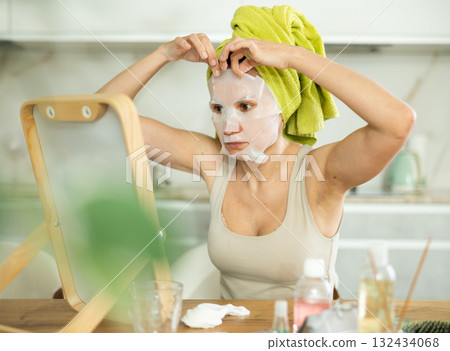 Woman in towel turban on head applying hydrating face mask Woman in towel turban on head applying hydrating face mask 132434068
