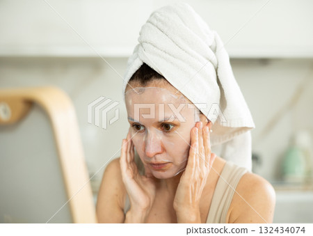 Woman in towel turban on head applying hydrating face mask 132434074