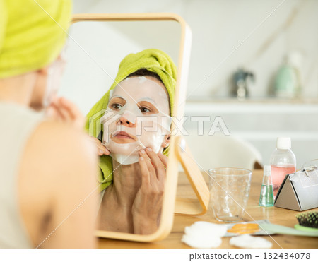 Woman with towel head wrap applying cosmetic face mask Woman with towel head wrap applying cosmetic face mask 132434078