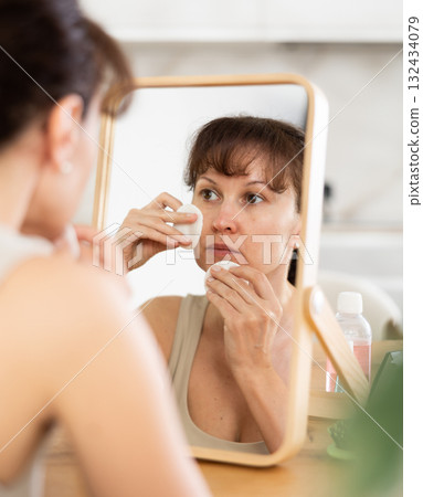 Woman cleansing face with cotton pads in front of mirror Woman cleansing face with cotton pads in front of mirror 132434079