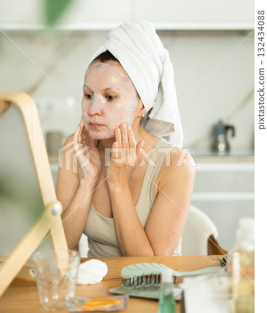 Woman in towel turban on head applying hydrating face mask Woman in towel turban on head applying hydrating face mask 132434088