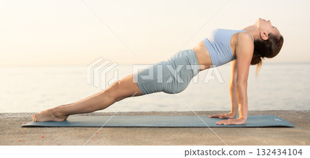 Near sea during sunset, girl performs reverse plank pose Near sea during sunset, girl performs reverse plank pose 132434104