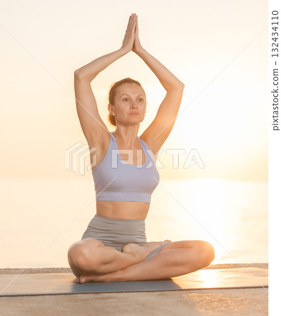 Near sea during sunset, girl performs variations of padmasana Near sea during sunset, girl performs variations of padmasana 132434110