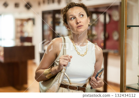 Woman curiously observing antique artifacts in historical museum Woman curiously observing antique artifacts in historical museum 132434112