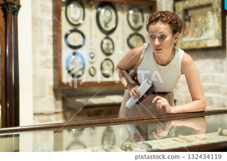 Woman with brochure in her hands examines exhibits in glass stands of historical museum 132434119