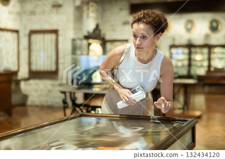 Woman examining antique artifacts within glass vitrine in museum 132434120