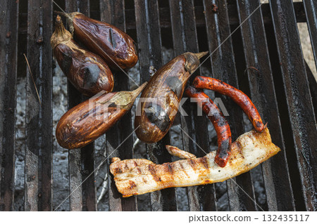 Grilled eggplants and sausages on a rustic barbecue grill 132435117