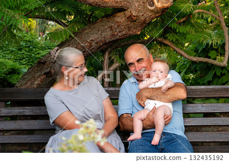 Senior couple enjoying moment with baby in green garden Senior couple enjoying moment with baby in green garden 132435192
