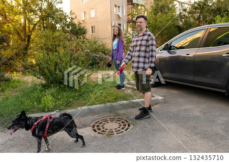 Father and daughter walking dog with leash near parked car Father and daughter walking dog with leash near parked car 132435710