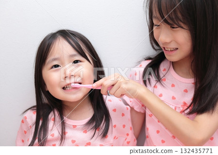 Two sisters, ages 4 and 10, brushing their teeth in pajamas 132435771