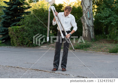Man unfolds tripod for telescope setup outdoors 132435927
