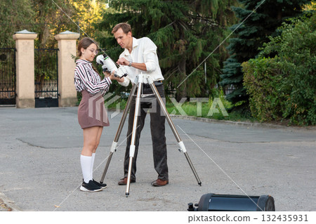 Teacher assists girl attaching telescope mount outdoors 132435931