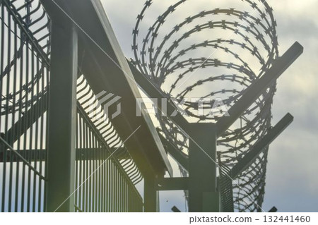Barbed wire on a high-security building. Barbed wire and solid wire fencing. Concepts for detention centers, military facilities, nuclear power plants, and defense against illegal migration. Barbed wire on a high-security building. Barbed wire and solid wire fencing. Concepts for detention centers, military facilities, nuclear power plants, and defense against illegal migration. 132441460