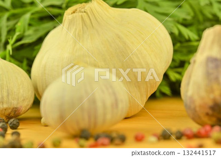 The bulbs of garlic, four-color pepper, and carrot tops on a wooden cutting board. The concept of culinary arts and vegetables in the home. Macro image, close-up. Garlic - species Allium sativum, is a The bulbs of garlic, four-color pepper, and carrot tops on a wooden cutting board. The concept of culinary arts and vegetables in the home. Macro image, close-up. Garlic - species Allium sativum, is a 132441517