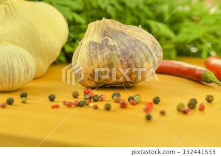 A bulb of garlic, red chili peppers, four-color pepper, and carrot tops on a wooden cutting board. The concept of cooking and vegetables in the home. Macro image, close-up. Garlic - Allium sativum is A bulb of garlic, red chili peppers, four-color pepper, and carrot tops on a wooden cutting board. The concept of cooking and vegetables in the home. Macro image, close-up. Garlic - Allium sativum is 132441533