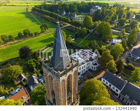 Aerial view of town with central Gothic style church, pointed steeple, red and gray rooftops, tree lined streets, and parked cars blending history with modern life. 132441990