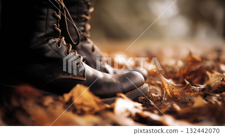 Close-up of black leather boots standing among dry autumn leaves on the ground in warm natural light 132442070