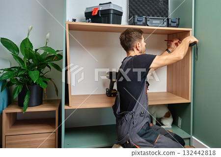 Man measuring wooden cabinet, using measuring tape and pencil to mark panel during home furniture assembly Man measuring wooden cabinet, using measuring tape and pencil to mark panel during home furniture assembly 132442818