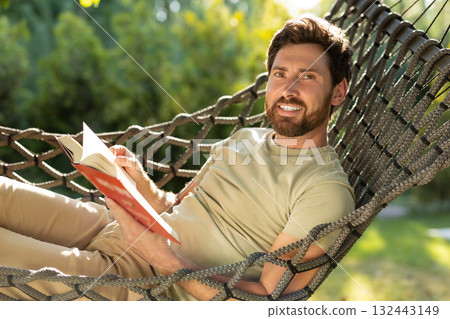 Caucasian bearded young man lying in hammock with a book in hands 132443149