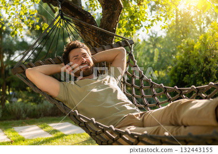 Bearded young man lying in a hammock and feeling relaxed Bearded young man lying in a hammock and feeling relaxed 132443155