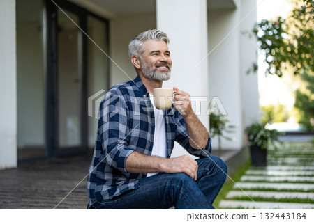Gray-haired mature man sitting in his house yard and having morning coffee 132443184