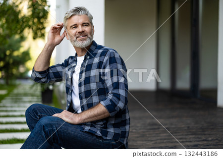 Gray-haired mature man sitting in his house yard and having morning coffee Gray-haired mature man sitting in his house yard and having morning coffee 132443186