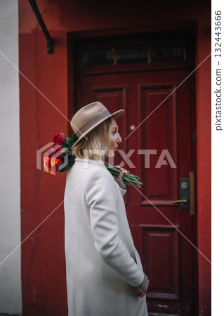 Woman holding flowers walks near red door in urban setting during daytime 132443666