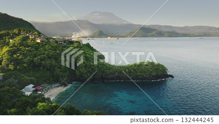 Aerial view secluded Bali Blue Lagoon beach with lush green hills, traditional coastal villages and tranquil turquoise water framed by Mount Agung. Tropical island landscape. Drone flight footage Aerial view secluded Bali Blue Lagoon beach with lush green hills, traditional coastal villages and tranquil turquoise water framed by Mount Agung. Tropical island landscape. Drone flight footage 132444245