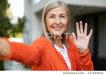 Mature pretty woman feeling excited and waving her hand while having a video call 132444642