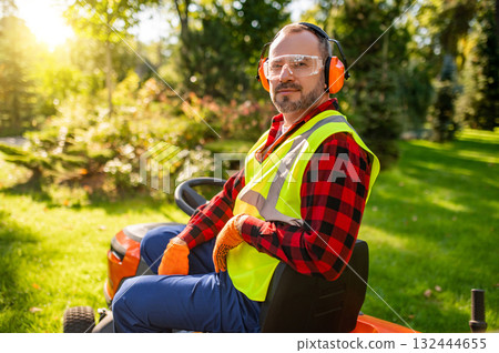 Landscaper mowing lawn in backyard wearing uniform and protective goggles 132444655