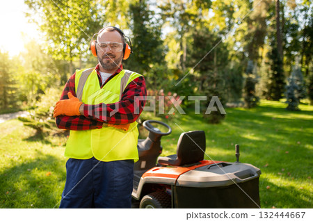 Gardener standing in sunny garden with lawnmower surrounded by green plants Gardener standing in sunny garden with lawnmower surrounded by green plants 132444667