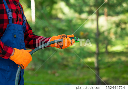 Male gardener standing among bushes performing irrigation work Male gardener standing among bushes performing irrigation work 132444724
