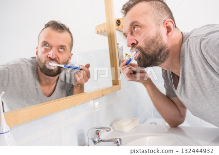 Man brushing his teeth in bathroom Man brushing his teeth in bathroom 132444932