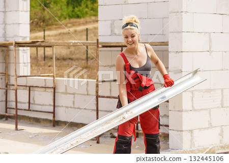 Woman carrying gutter on construction site 132445106