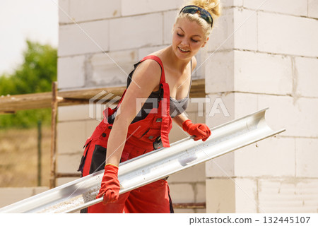 Woman carrying gutter on construction site Woman carrying gutter on construction site 132445107