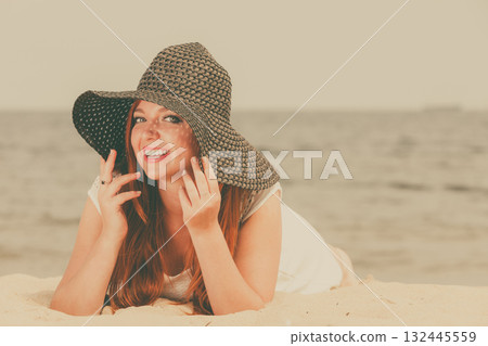 Redhead woman wearing sun hat lying on beach 132445559