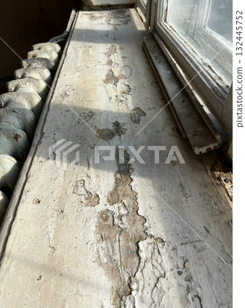 Old wooden window sill, peeling from paint, next to a cast-iron radiator Old wooden window sill, peeling from paint, next to a cast-iron radiator 132445752
