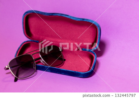 Elegant sunglasses with dark lenses on velvet case set against pink purple gradient background 132445797