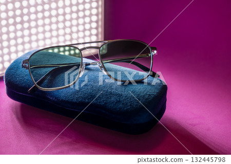Elegant tinted sunglasses on velvet case with dramatic retro light and shadow over magenta base 132445798