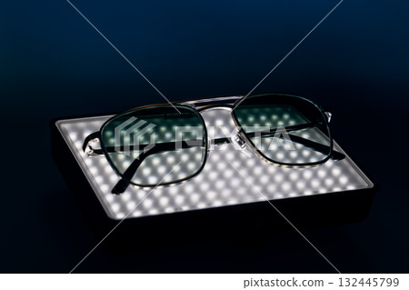 Stylish tinted eyewear displayed on lit surface with deep blue futuristic tones and retro feel 132445799